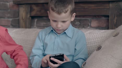 blond junior schoolboy surfs attentively internet on phone