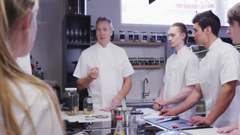 professional caucasian male chef in a restaurant kitchen teaching a group of trainee chefs