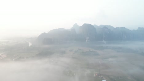 aerial drone shot of misty morning fog over river in vang vieng, the adventure capital of laos