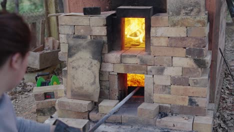 una mujer tiende a las brasas en su horno de leña en preparación para disparar sus ollas - artesano de cerámica tradicional