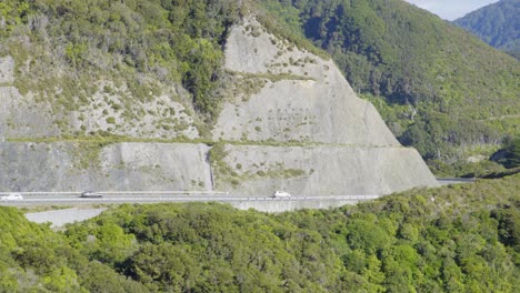 Eine-Totale-Von-Autos,-Die-Auf-Einer-Bergstraße-Neben-Einem-Großen-Straßeneinschnitt-Fahren