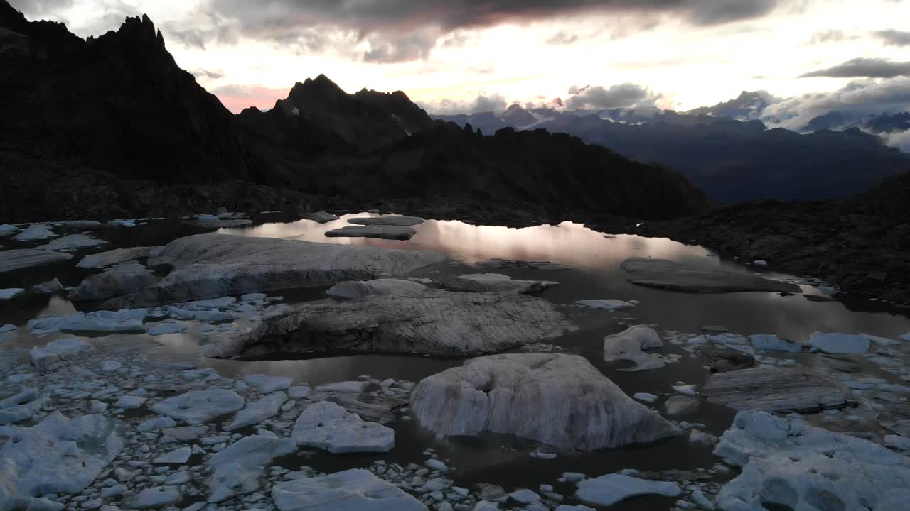 sobrevuelo aéreo sobre un lago glaciar lleno de icebergs derretidos en partes remotas de los alpes suizos durante la puesta de sol