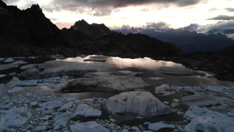 Aerial-flyover-above-a-glacier-lake-full-of-melted-icebergs-in-remote-parts-of-the-Swiss-Alps-during-sunset