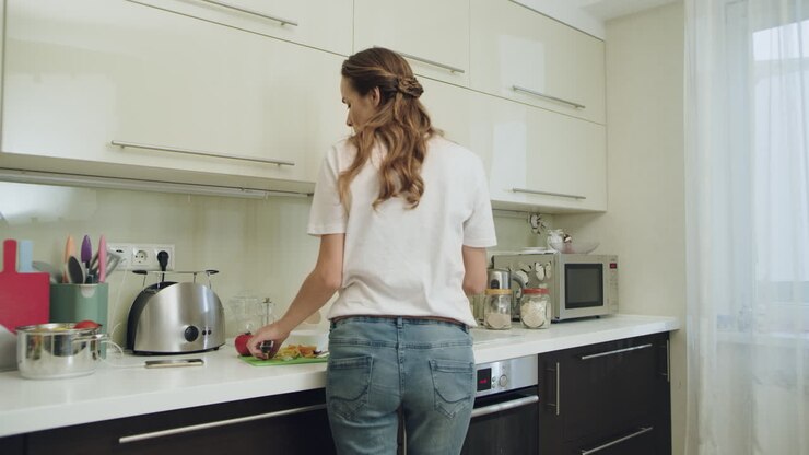 Giovane donna che si diverte a ballare da sola. Donna che prepara la cena nella cucina di casa.