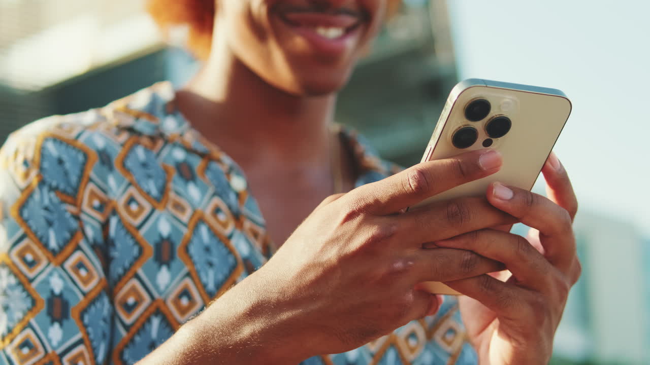 Mladý muž se usmívá při používání smartphonu venku