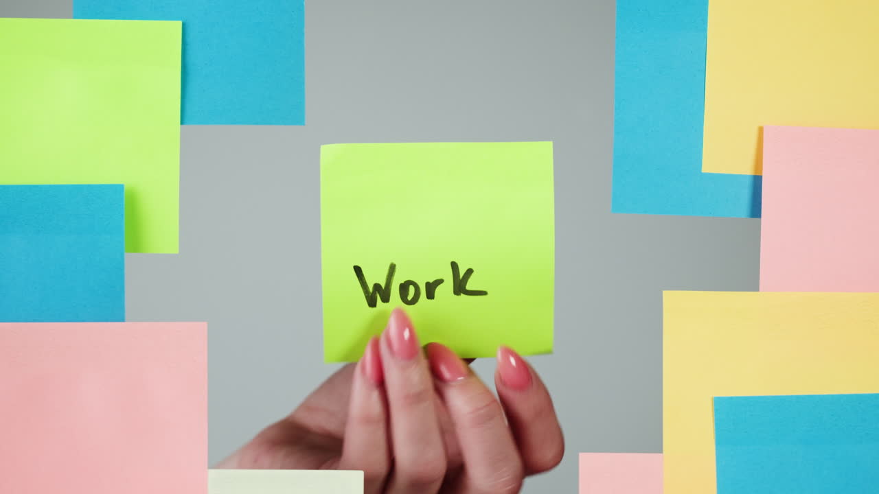 Woman's Hand Removing 'Work' Sticky Note from Wall