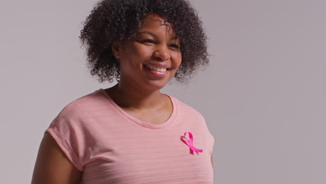 Studio-Portrait-Of-Smiling-Mid-Adult-Woman-Wearing-Pink-Breast-Cancer-Awareness-Ribbon-Against-White-Background-1