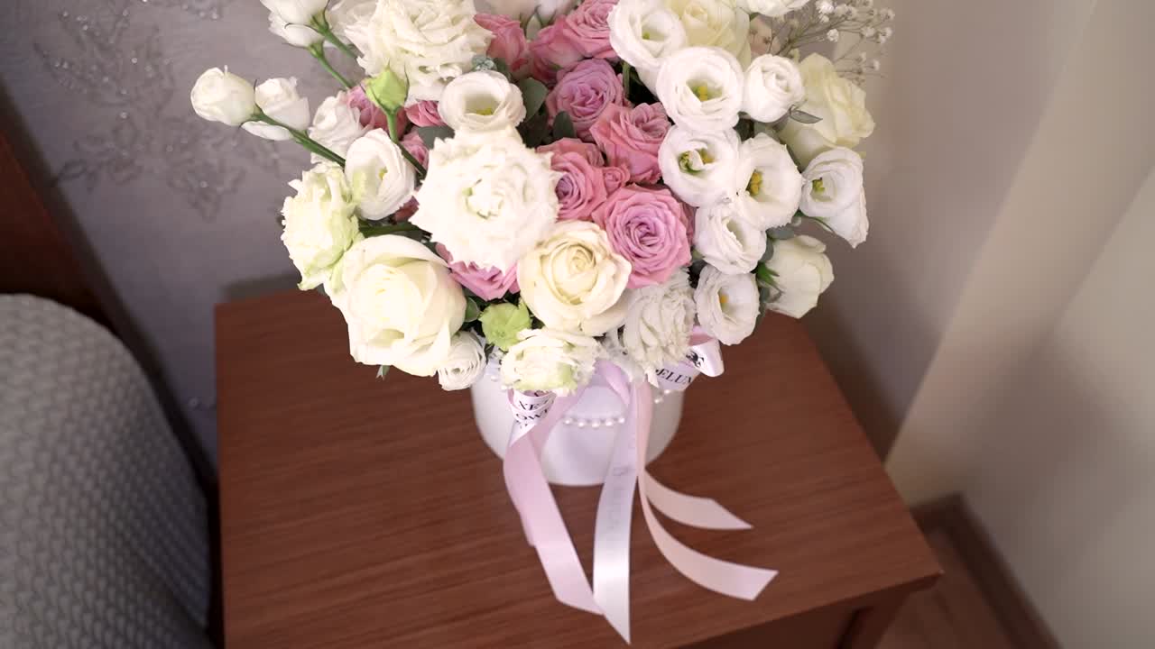 Un bouquet pieno di vari fiori è appoggiato su un tavolo. La composizione include rose bianche e rosa tra gli altri fiori. La stanza è ben illuminata.