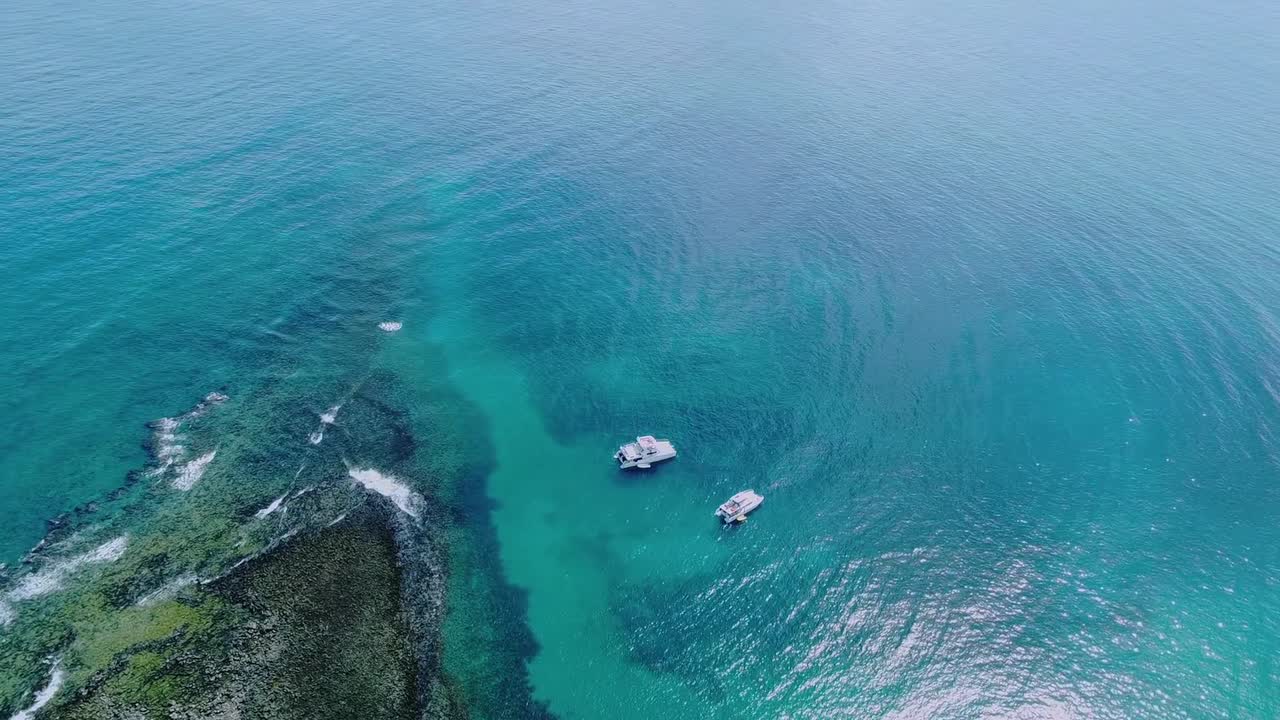Barche sopra la barriera corallina nel Parco Nazionale Marino di Abrolhos vicino a Caravelas, Bahia, Brasile, con formazioni a chapeirão in acque limpide dell'Atlantico, volo lento in avanti con drone dall'alto.