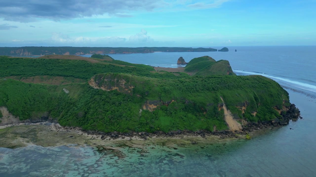 Vista della costa dell'isola di Lombok che mostra colline verdi che incontrano l'oceano blu chiaro con barriere coralline poco profonde e onde leggere. Panoramica aerea fluida con drone in volo inverso.