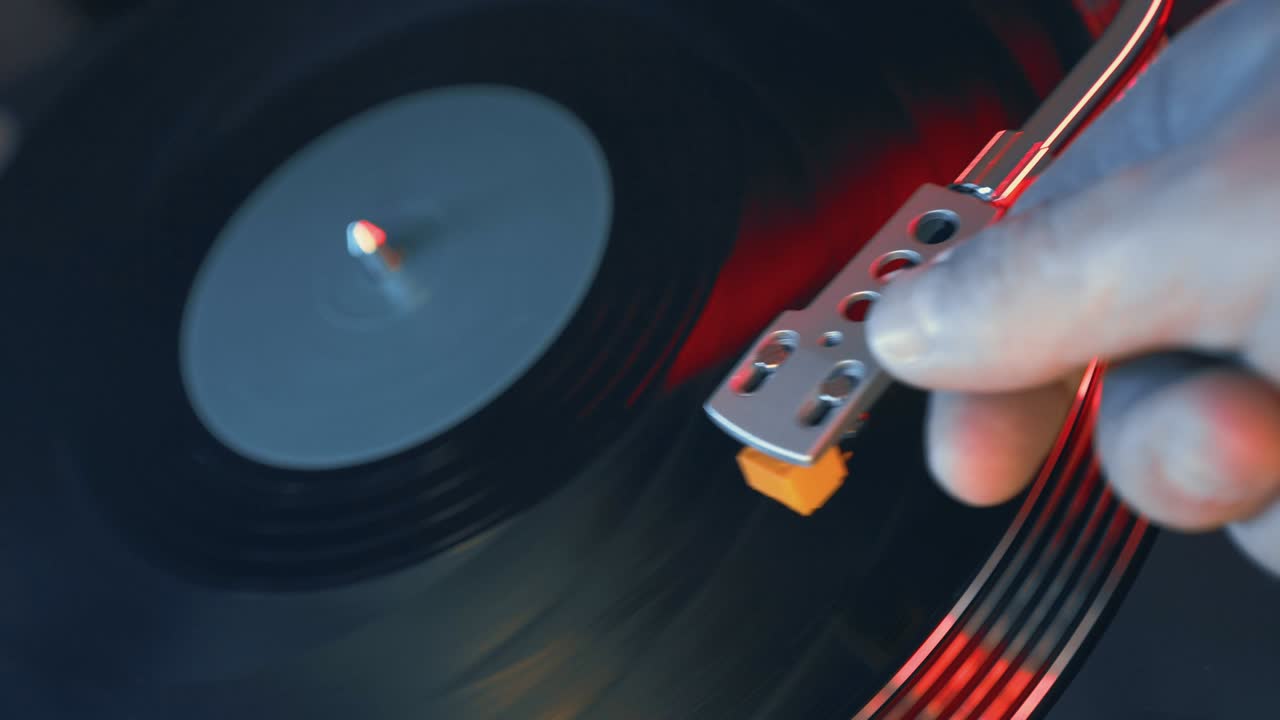 빨간색과 파란색의 불빛을 배경으로 플레이어 비닐 턴테이블 클로즈업. 젊은이의 손은 부드럽게 회전 판에 바늘을 배치. 청소년 학생의 파티에서 dj