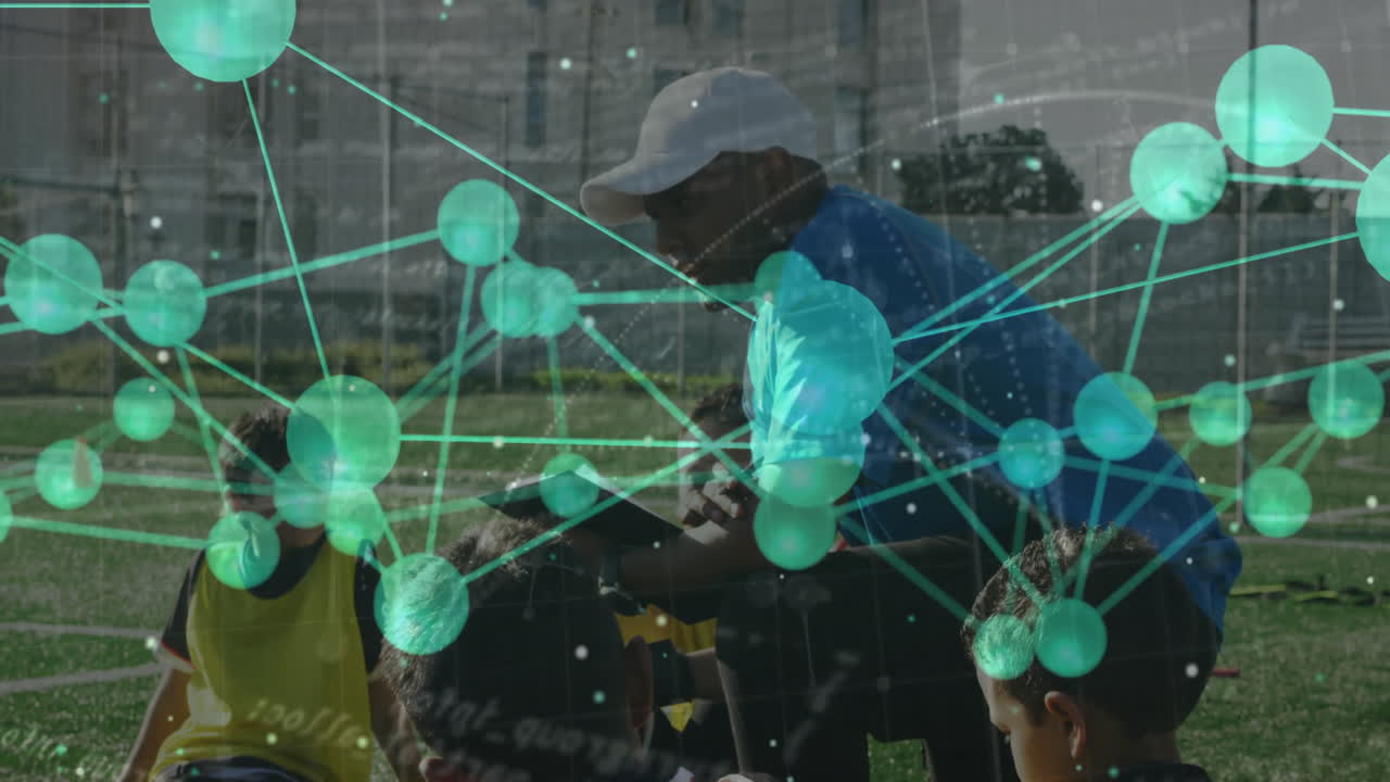Coach kneeling on field instructing boys with orange cones and green overlay in sports education