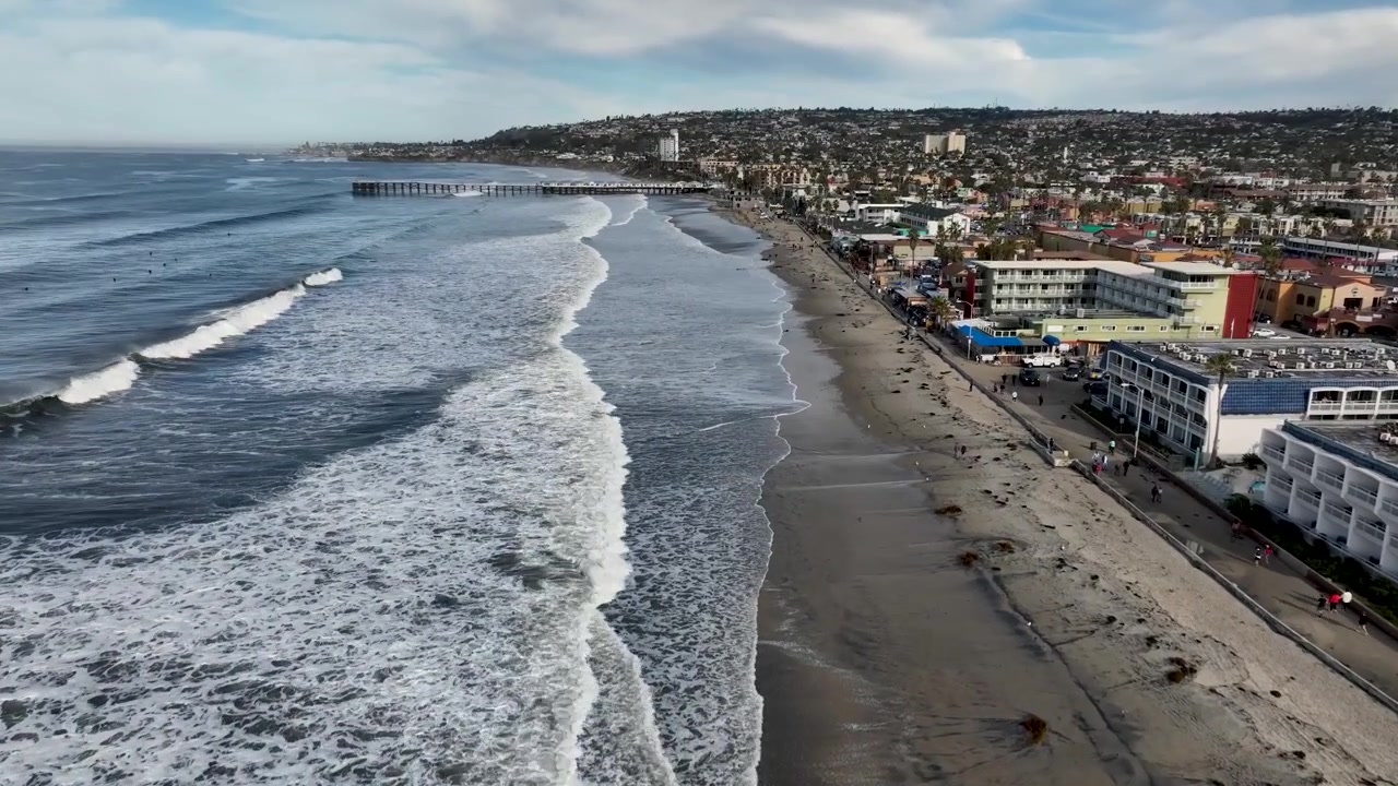 Veduta aerea mattutina delle maree reali che si riversano lungo la costa di Pacific Beach a San Diego, con onde e paesaggio costiero.