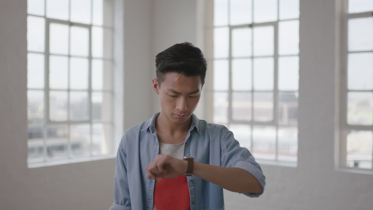 아파트 창문 배경에 스마트 워치 모바일 기술을 사용하여 문자 메시지를 탐색하는 젊은 아시아 남성 학생의 포트레이트