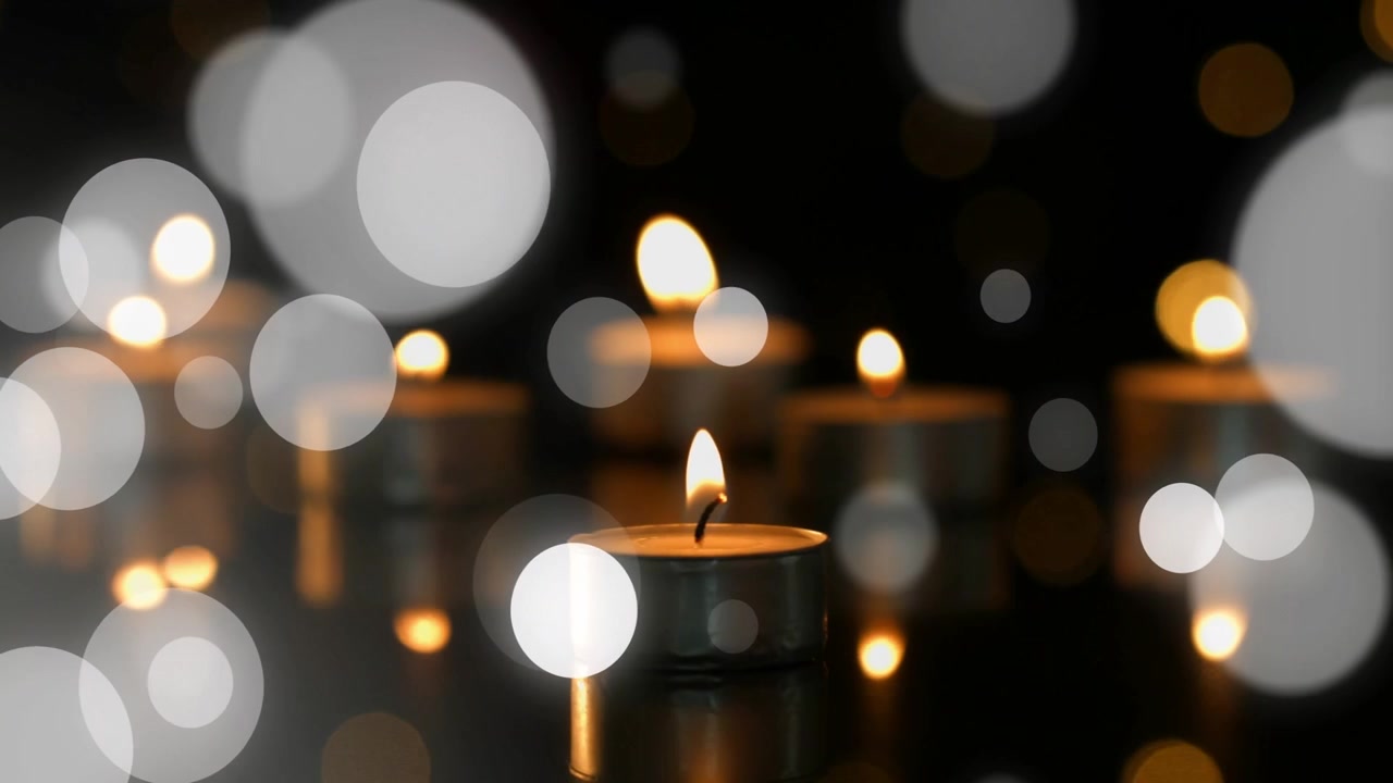 Lente ajustando o foco, revelando velas tealight de metal refletindo enquanto bokeh âmbar se desloca para um close-up