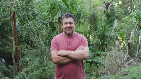 lächelnder kaukasischer männlicher gärtner mit gekreuzten händen, der die kamera im gartenzentrum ansieht