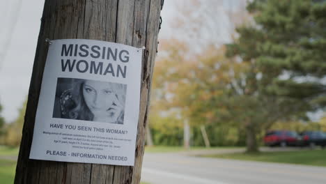 an advertisement for a missing young woman hangs on a pole near the road