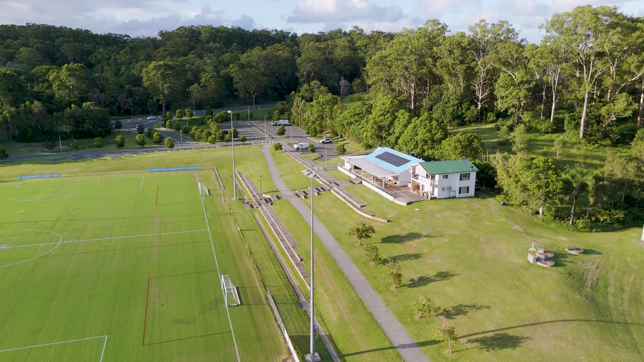 Drone footage captures soccer fields and a clubhouse amidst lush greenery under clear skies