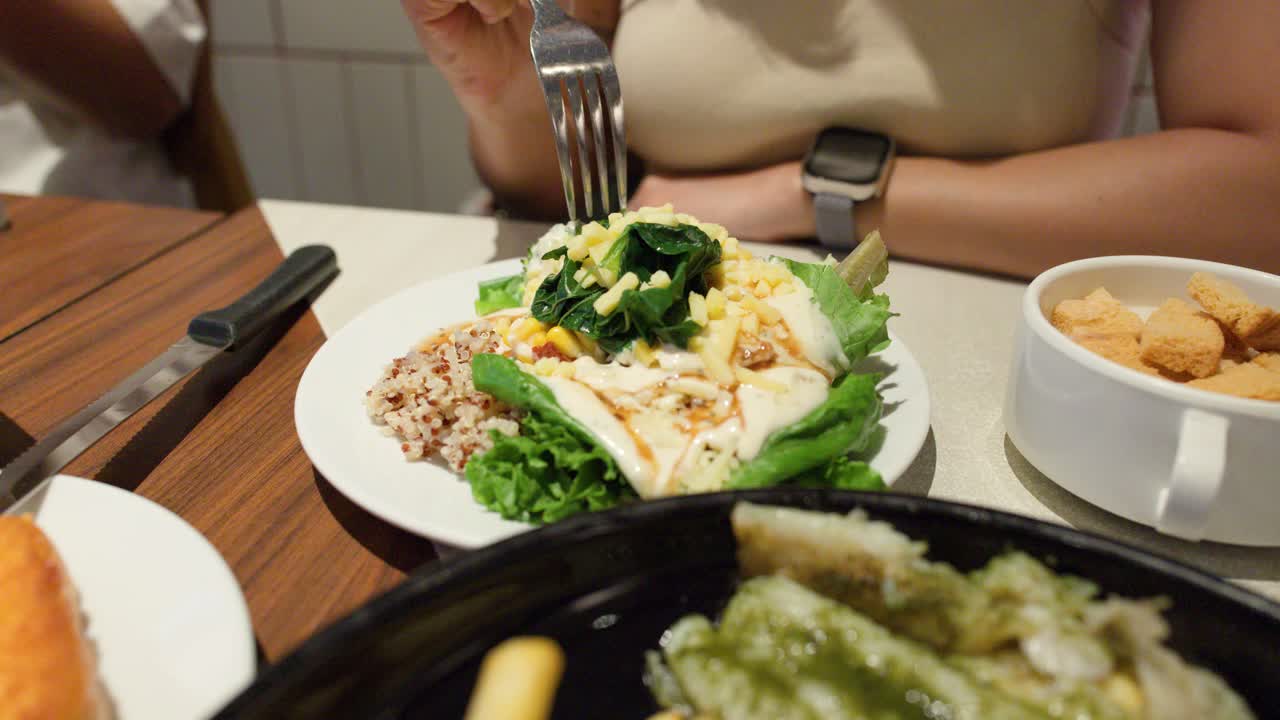 Close-up de uma mulher comendo salada de quinoa com verduras frescas em um restaurante casual com iluminação aconchegante