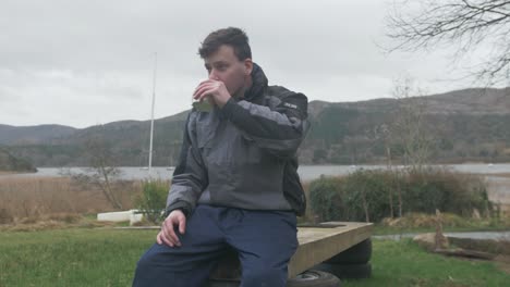 young man drinks coffee taking break from landscaping job, medium shot