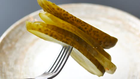 primer plano de un tenedor con una pila de rebanadas de pepinillos de eneldo en un plato.