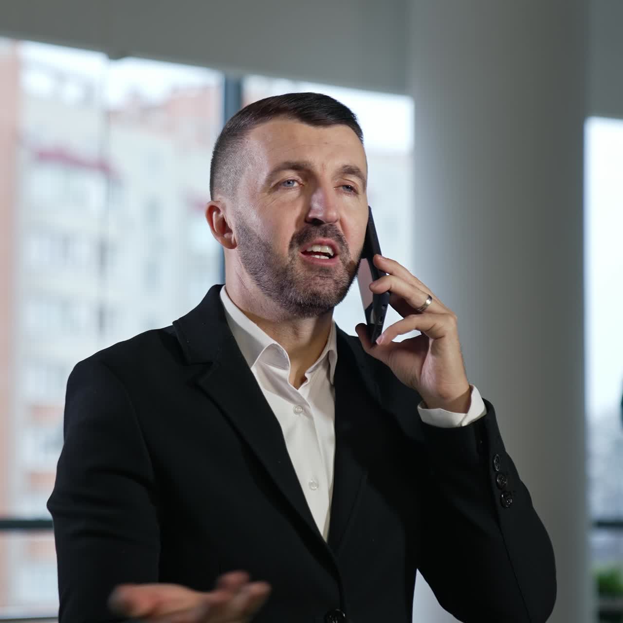 Selvsikker kaukasisk forretningsmann i middelalderen som har en samtale over smarttelefonen. Mannen snakker og peker fremover med hånden. Uskarp bakgrunn