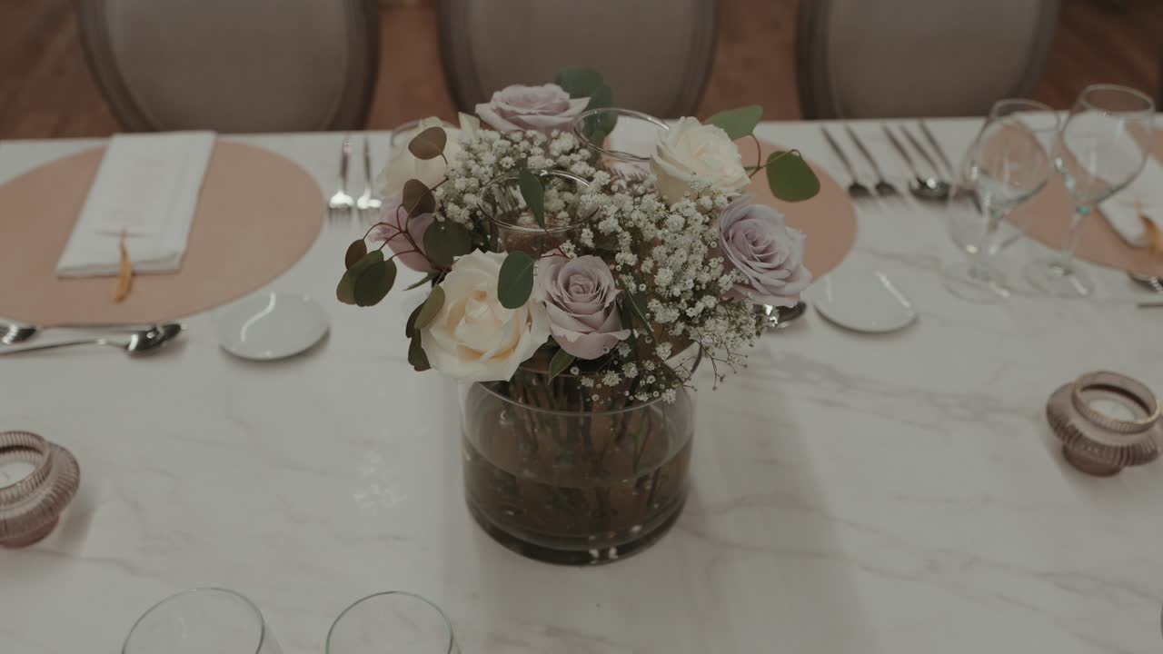 soft pastel roses and greenery arranged in a glass vase for a refined table setting