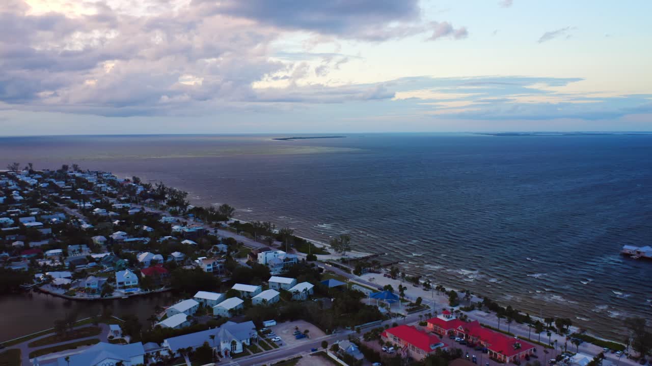 Overlooking the northern edge of Anna Maria Island, calm blue Gulf waters stretch to the horizon as pastel houses and red rooftops glow beneath a peaceful evening sky