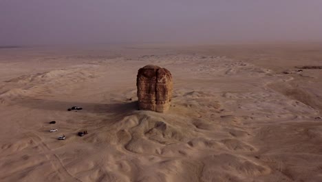 Group-of-vehicles-stopped-at-lonely-sandstone-cliff-in-middle-of-desert