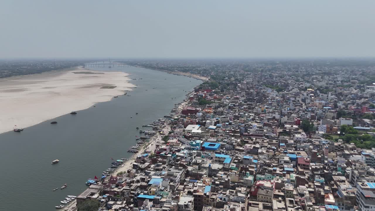 High-angle view of the Ganges River as it cuts through the heart of Varanasi, framed by tightly packed neighborhoods and bustling marketplaces.