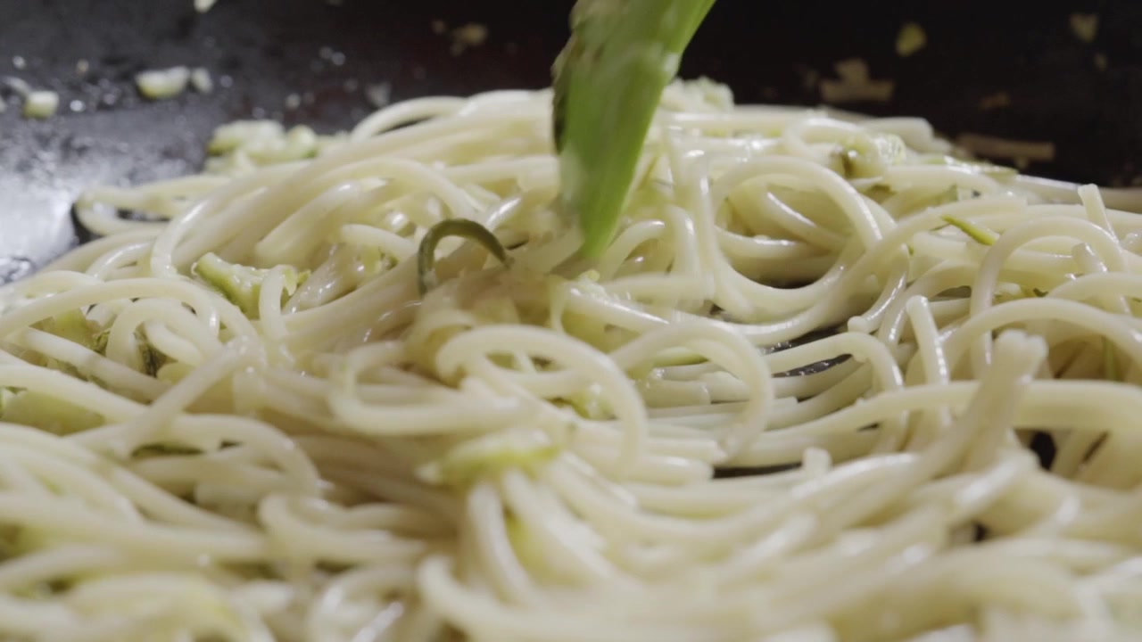 Primo piano di spaghetti che cuociono in salsa cremosa mentre vengono mescolati in una padella da cucina durante la preparazione del cibo in una cucina messicana