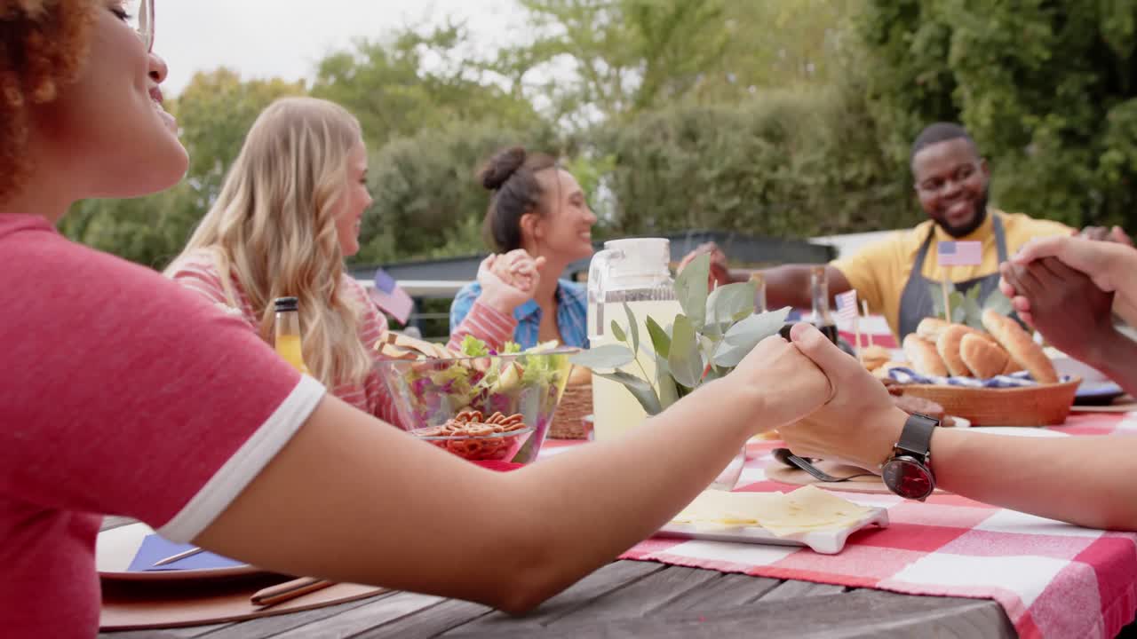 grupo diverso de amigos tomados de la mano y diciendo oración en la mesa de la cena en el jardín, cámara lenta