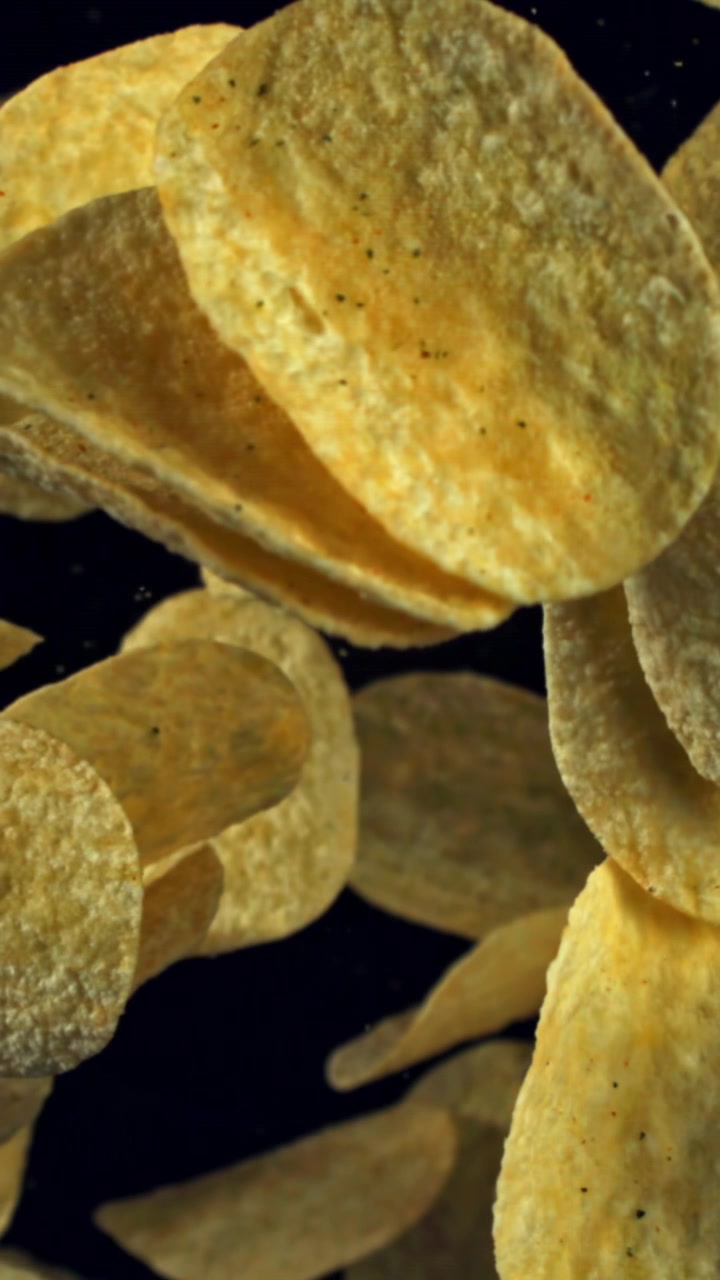 Golden Potato Chips Falling in Slow Motion on Black Background