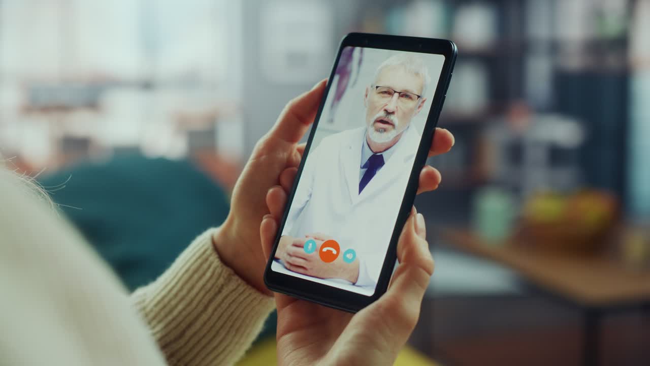 un primer plano de una mujer hablando en una llamada de video con su médico de familia senior en un teléfono inteligente desde la sala de estar. una mujer con malos sentimientos haciendo una llamada desde casa con un médico a través de internet.