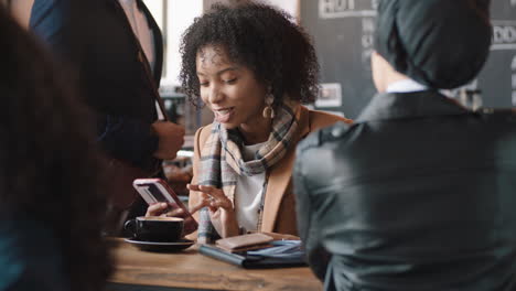 Schöne-Afroamerikanische-Frau-Nutzt-Ihr-Smartphone-Im-Café-Und-Schreibt-SMS,-Teilt-Nachrichten-In-Sozialen-Medien-Und-Genießt-Mobile-Technologie,-Während-Sie-Mit-Einem-Freund-In-Einem-Belebten-Restaurant-Chattet