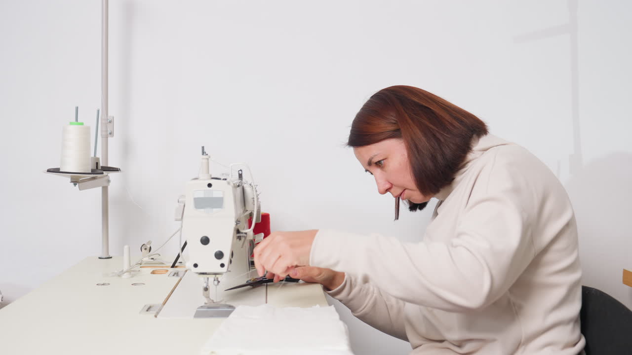 Seamstress carefully adjusting thread to needle on sewing machine, leaning with intense focus, demonstrating professional technique in minimal environment, highlighting skill, and garment preparation