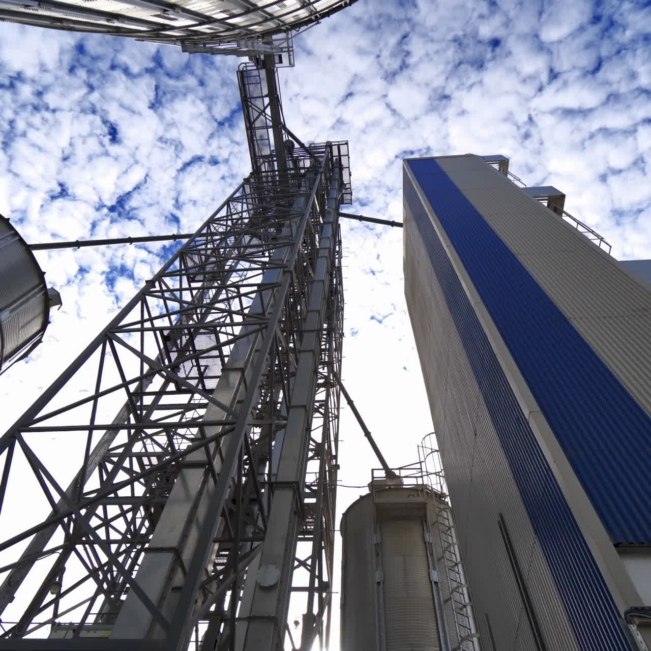 Metal construction on a modern industrial plant. Large grain elevators on beautiful sky background. View from below.