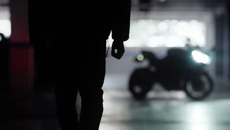 silhouette young man walks up to his black motorbike and climbs onto it and revs throttle, cinematic slow motion wide shot