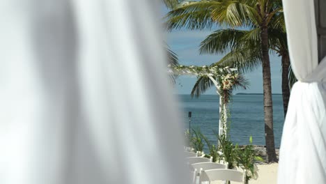 Toma-Panorámica-Lenta-Que-Revela-Un-Escenario-De-Ceremonia-Vacío-En-El-Lugar-De-La-Boda-Con-Agua-De-Playa-Y-Barcos-Al-Fondo