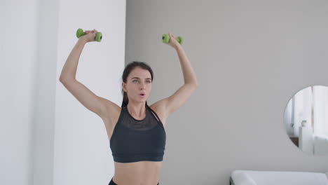 raise the dumbbells over your head performing exercises for the shoulders. training at home in the apartment. a brunette woman with long hair and a beautiful figure