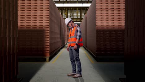 full body side view of asian male engineer with safety helmet having a headache while working with red brick packed in stacks are stored