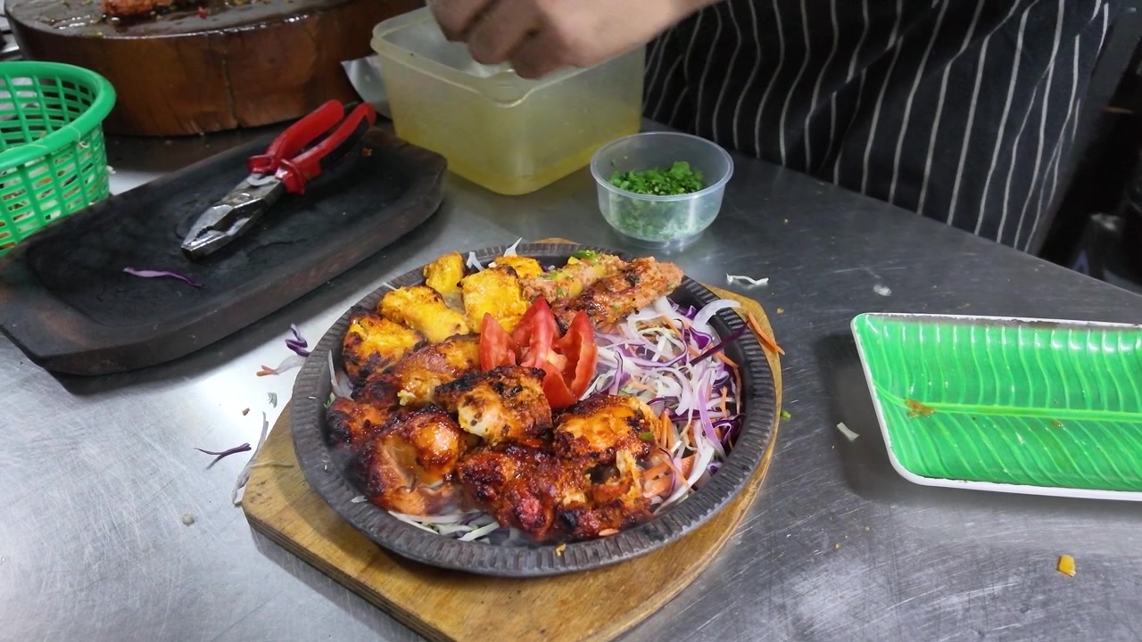 Tangan koki menata ayam tandoori panas di atas piring sizzler berasap di dapur.