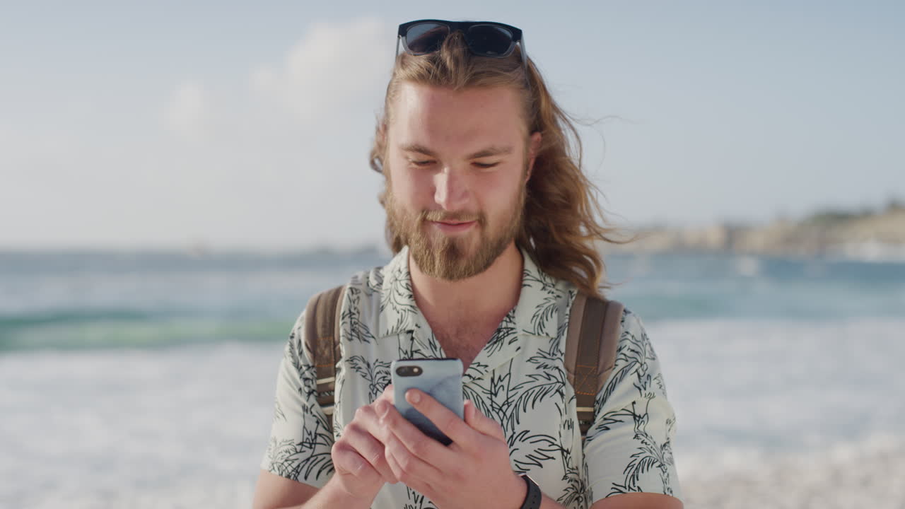 ritratto di un bel giovane che scrive messaggi, naviga con lo smartphone, si sente connesso all'estate sulla spiaggia sull'oceano.