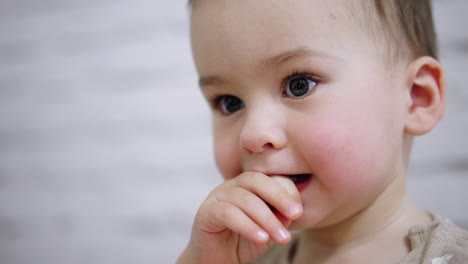 beautiful caucasian toddler keeping fingers in mouth. baby chews his fingers while is focused on something else. close up.