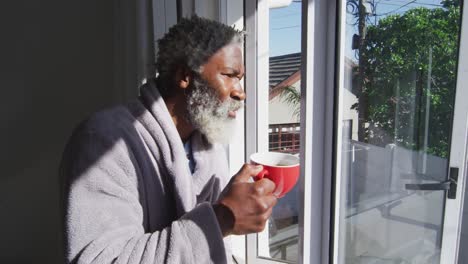 senior man drinking coffee while looking out of window at home