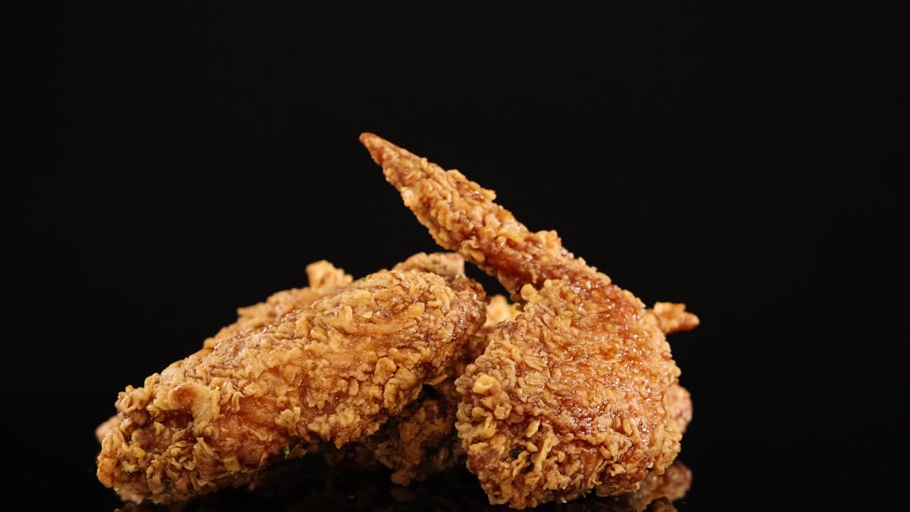 Golden-brown fried chicken wings rotate smoothly on a glossy black surface, illuminated by soft studio lighting for a mouthwatering, high-contrast food presentation
