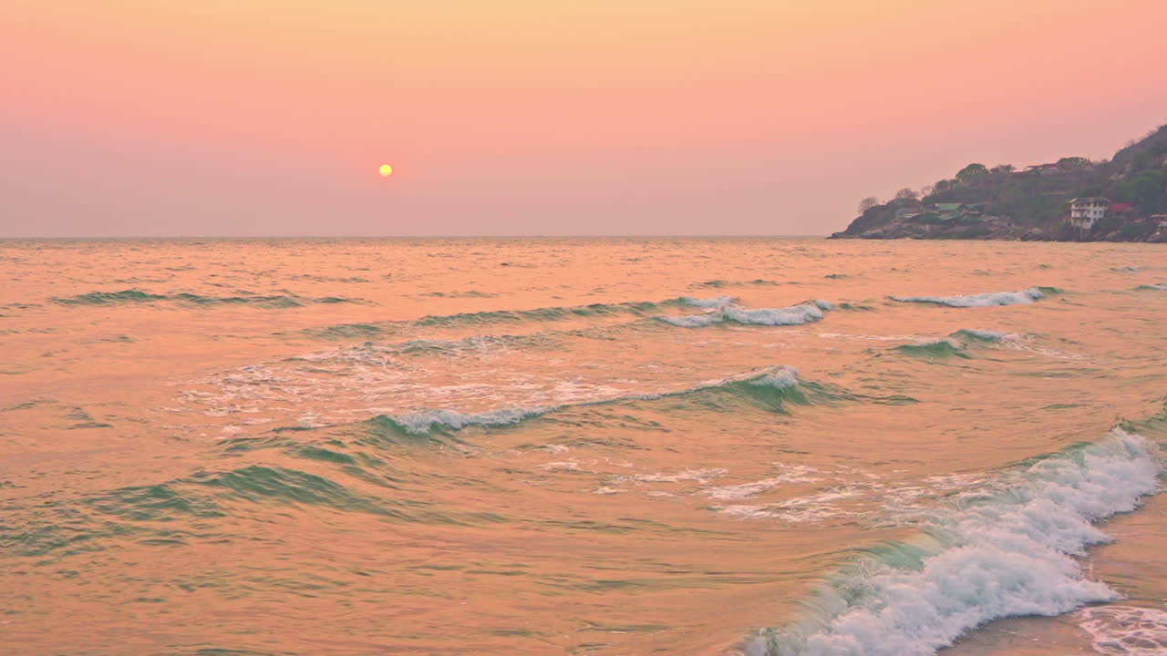 Pan right of tropical island coastline waves during a golden sunset