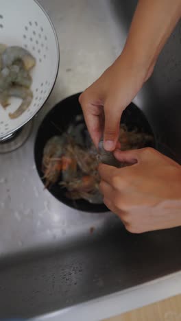 hands peeling raw shrimp in a kitchen sink