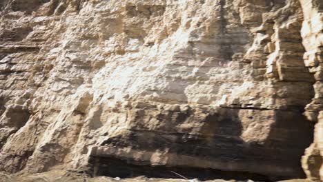 Driving-next-to-a-sandstone-rock-wall-on-the-highway,-handheld