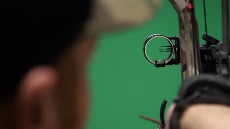 bowhunter aiming his archery bow on a green screen background for superimposing targets